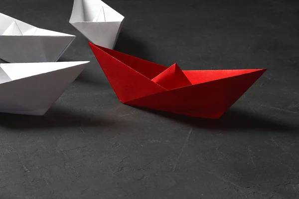 Business leadership Concept, Paper Boat, the key opinion Leader, the concept of influence. One red paper boat as the Leader, leading in the direction of the white ships on a gray concrete background,c