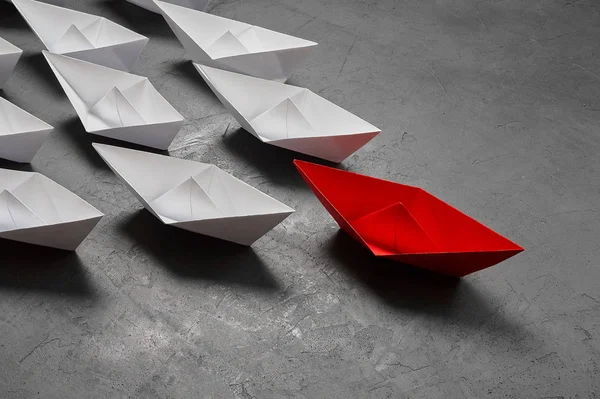 İş liderliği kavramı, Paper Boat, anahtar fikir lideri, nüfuz kavramı. Lider olarak bir kırmızı kağıt tekne, gri beton arka planda beyaz gemilere doğru gidiyor.