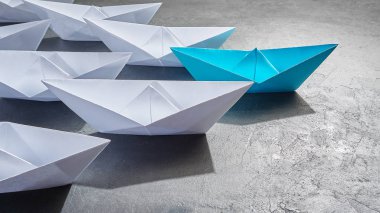 İş liderliği kavramı, Paper Boat, anahtar fikir lideri, nüfuz kavramı. Lider olarak mavi kağıttan bir tekne, gri beton arka planda beyaz gemilere doğru gidiyor.,