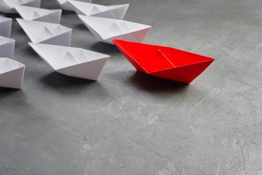 İş liderliği kavramı, Paper Boat, anahtar fikir lideri, nüfuz kavramı. Lider olarak bir kırmızı kağıt tekne, gri beton arka planda beyaz gemilere doğru gidiyor.