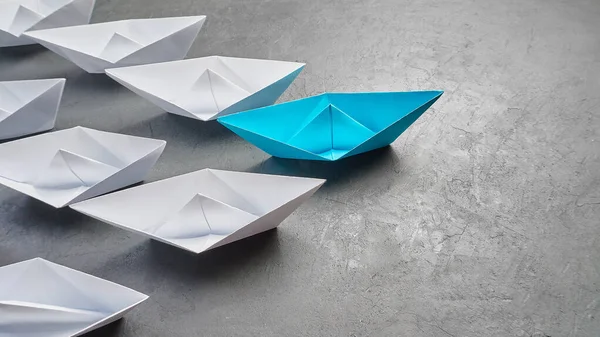 Επιχειρησιακή ηγεσία Concept, Paper Boat, η βασική άποψη Leader, η έννοια της επιρροής. Ένα μπλε χάρτινο σκάφος ως αρχηγός, που οδηγεί προς την κατεύθυνση των λευκών πλοίων σε γκρι φόντο από τσιμέντο., — Φωτογραφία Αρχείου