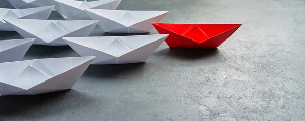 İş liderliği kavramı, Paper Boat, anahtar fikir lideri, nüfuz kavramı. Lider olarak bir kırmızı kağıt tekne, gri beton arka planda beyaz gemilere doğru gidiyor.