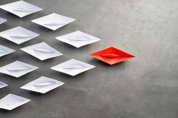 Business leadership Concept,key opinion Leader, the concept of influence. One red paper boat as the Leader, leading in the direction of the white ships on a gray concrete background,copy space,flat la