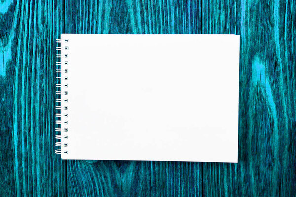 white office Notepad lies on a bright blue colored wooden background, minimalistic design, top view, flat lay, copy space