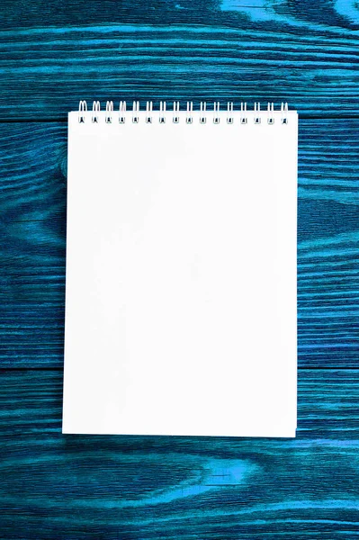 Λευκό γραφείο Notepad βρίσκεται σε ένα φωτεινό μπλε χρώμα ξύλινο υπόβαθρο, μινιμαλιστικό σχεδιασμό, κορυφαία άποψη, επίπεδη lay, αντίγραφο χώρου — Φωτογραφία Αρχείου