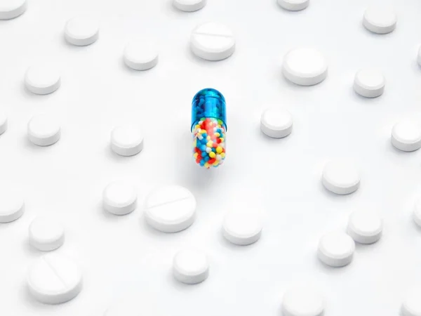 Conceito de pílula mágica. Uma cápsula grande comprimido com enchimento multi-colorido está no centro de comprimidos brancos em um fundo . — Fotografia de Stock
