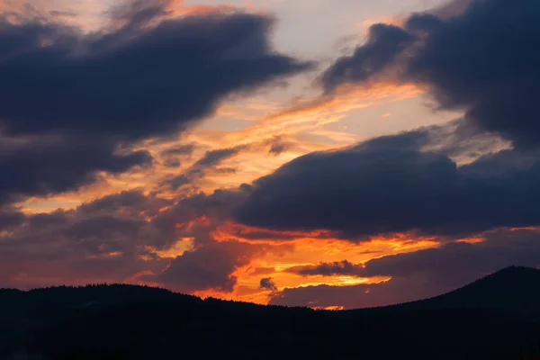 cloudy sky at sunset with a dramatic looking sunset over forested hills