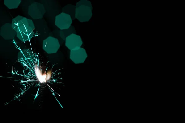 Sparkler in turquoise and white light on a black background.