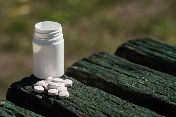 White  pills lie on an old bench. Pills or tablets closeup with bokeh. Concept photo on theme Coronavirus and Covid-19.