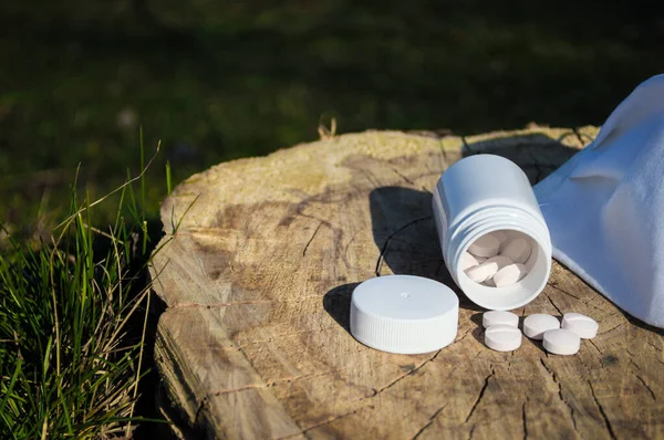 White jar and white pills with mask lie on a stump. Pills or tablets closeup with bokeh. Concept photo on theme Coronavirus and Covid-19.