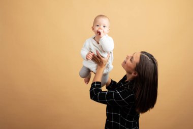 Genç ve enerjik bir anne bebeğini turuncu arka planda kucaklayıp öper.