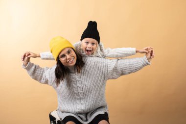 Genç ve enerjik bir anne, turuncu bir arka planda oğluna sarılıp onu öper.