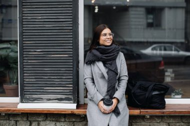 Gözlüklü genç bir kadının portresi. Genç bir iş kadını bir kafenin penceresinde duruyor ve kahve içiyor.