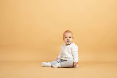 Bir bebek turuncu arka planda oturur ve kameraya bakar.