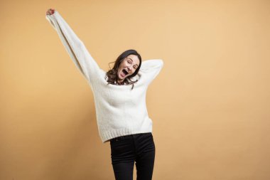 İzole edilmiş turuncu arka planda poz veren beyaz kazaklı güzel bir kadının görüntüsü farklı duyguları gösteriyor.