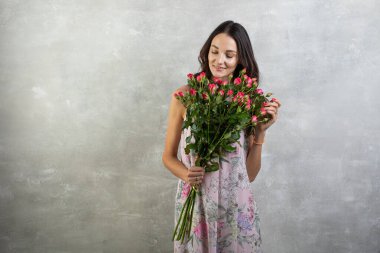 Elinde gül buketi tutan yaz elbisesi içindeki çekici genç bir kadının yakın plan portresi.
