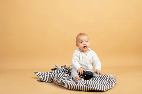 Un bébé est assis sur un fond gris orangé à carreaux avec un réveil dans ses mains — Photo
