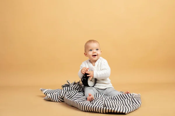 Un bébé est assis sur un fond gris orangé à carreaux avec un réveil dans ses mains — Photo