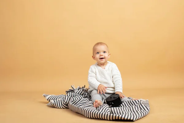 Un bébé est assis sur un fond gris orangé à carreaux avec un réveil dans ses mains — Photo