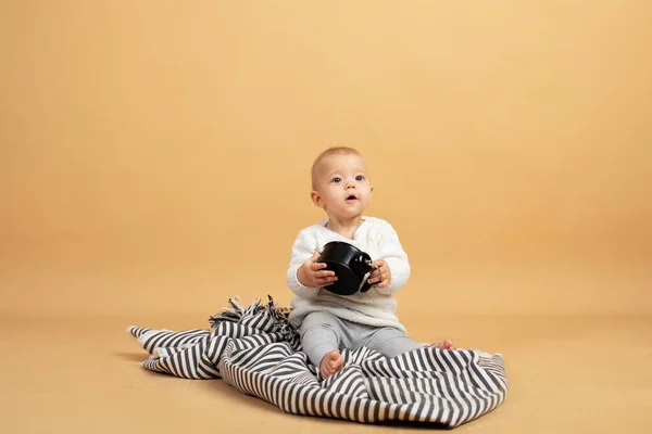 Un bébé est assis sur un fond gris orangé à carreaux avec un réveil dans ses mains — Photo