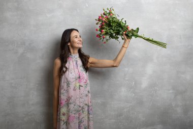 Elinde gül buketi tutan yaz elbisesi içindeki çekici genç bir kadının yakın plan portresi.