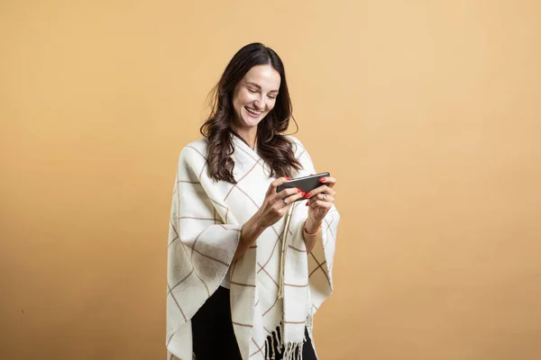 Изображение шокированной молодой красивой женщины, позирующей на фоне оранжевой стены, играющей в игры на мобильном телефоне — стоковое фото