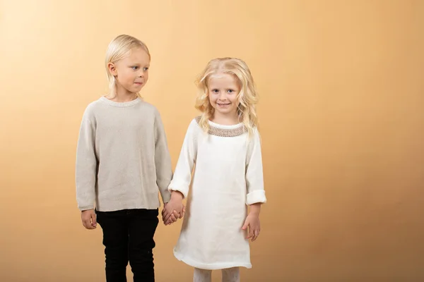 Une petite fille dans une robe blanche tricotée et un chapeau noir et un garçon dans un pull. Les enfants se tiennent la main — Photo