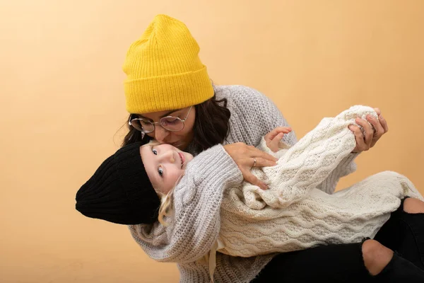 A young and energetic mother hugs and kisses her daughter on an orange background — Stock Photo, Image