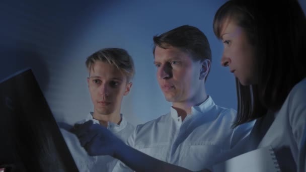 Trois médecins regardent ensemble une photo radiographique d'un patient. Travail conjoint de l'équipe de médecins de la clinique. Les médecins travaillent avec les stagiaires . — Video