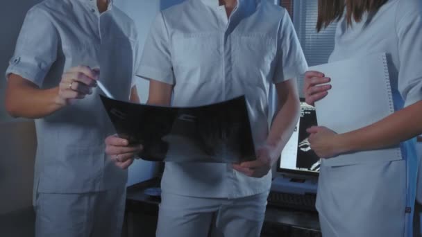 Τρεις γιατροί κοιτάζουν μια ακτινογραφία ενός ασθενή μαζί. — Αρχείο Βίντεο