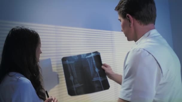 Två läkare undersöker röntgenbilden. Doktorn flickan och mannen diskuterar diagnosen. — Stockvideo