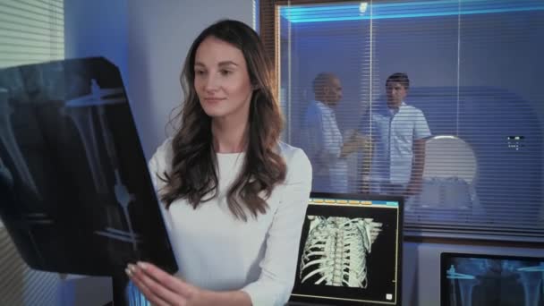 Una foto de una hermosa joven doctora. El médico está de pie en la sala de tomografía y estudiando la radiografía. Profesionales en el trabajo . — Vídeo de stock