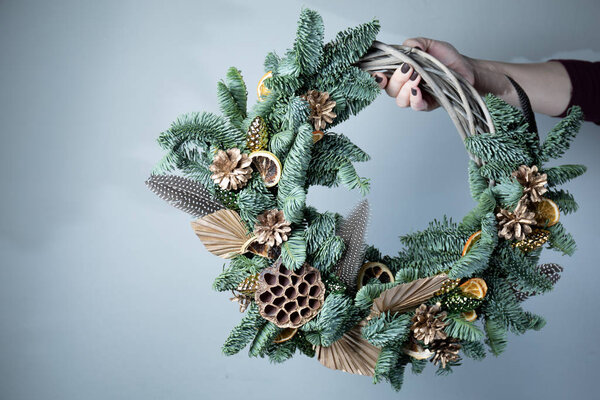 Крупным планом флористы держат рождественский венок с еловыми ветвями и шишками на столе
.