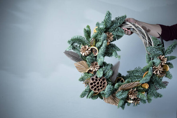Крупным планом флористы держат рождественский венок с еловыми ветвями и шишками на столе
.