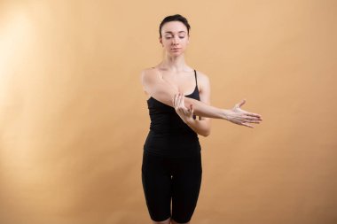 Beyaz atlet giyen güzel bir kadının portresi turuncu arka planda çalışıyor, esneme hareketleri yapıyor..