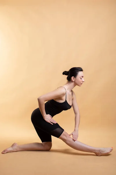 Retrato de vista lateral de una hermosa mujer joven con camiseta blanca haciendo ejercicio sobre fondo naranja, haciendo estiramiento . — Foto de Stock