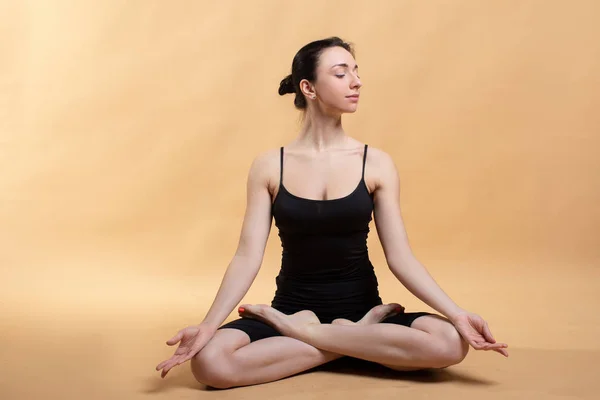 Side view portrait of beautiful young woman wearing white tank top working out against orange background, doing stretching. — Stock Photo, Image