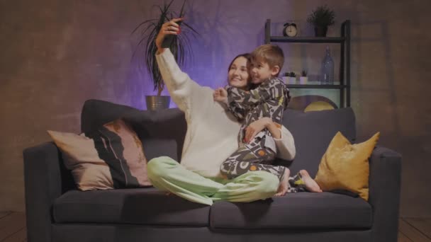 Νεαρή μητέρα και γιος κάθονται στον καναπέ σε ένα άνετο δωμάτιο και βγάζουν μια σέλφι — Αρχείο Βίντεο