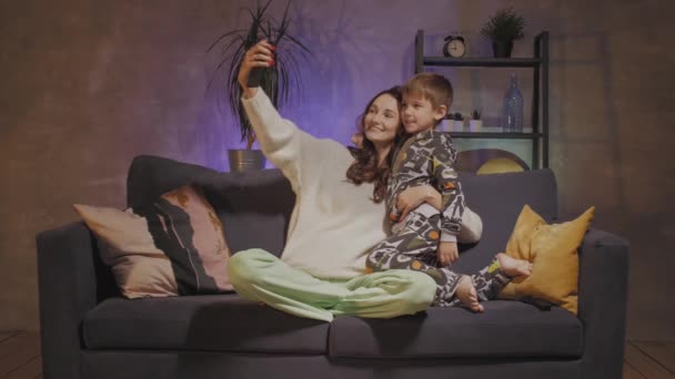 Giovane madre e figlio seduti sul divano in una stanza accogliente e farsi un selfie — Video Stock
