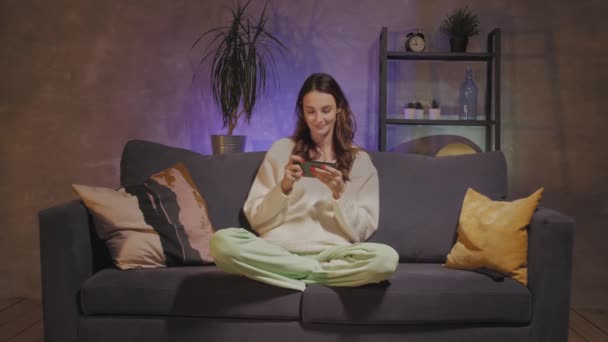 Mladá matka a syn sedí na gauči v útulném pokoji a hrají si na telefonu — Stock video