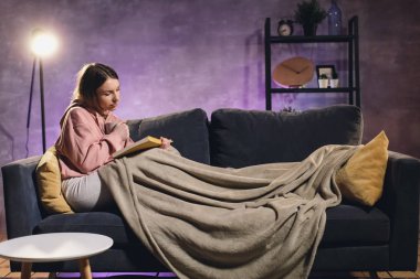 Kitap okuyan genç bir kız. Kız kanepede yatıyor. Samimi bir oda. Kız rüyaları