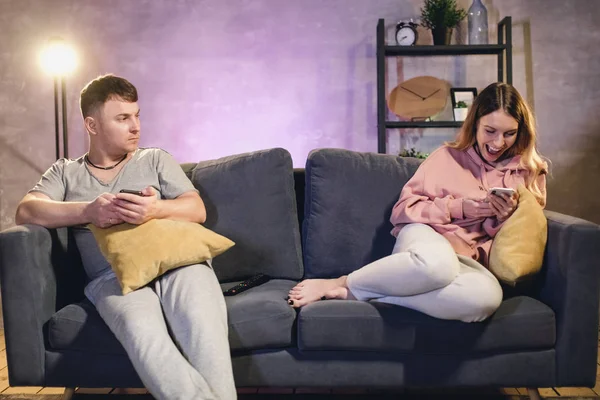 Un hombre y una mujer están sentados en el sofá y mandando mensajes en sus teléfonos. — Foto de Stock