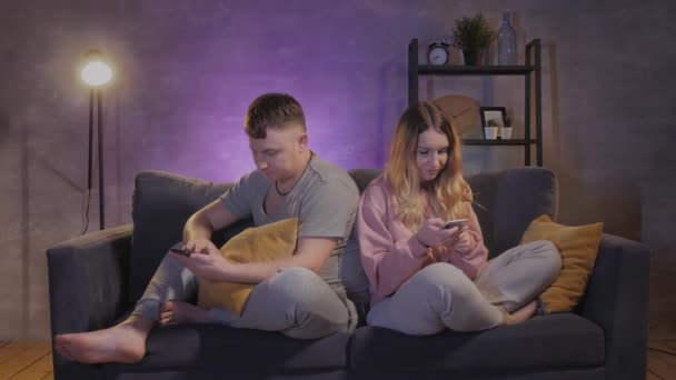 Un uomo e una donna sono seduti sul divano e messaggiano sui loro telefoni — Video Stock