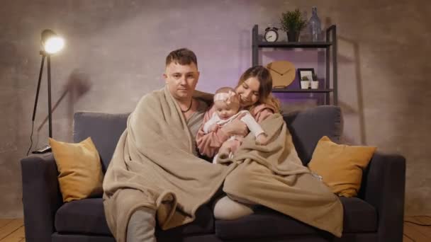 En ung familj sitter i soffan och tittar på Tv. Mamma, pappa och dotter är lyckliga. — Stockvideo