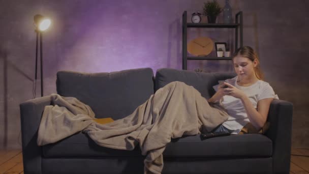 Giovane bella ragazza sdraiata sul divano e scrivere messaggi al telefono — Video Stock