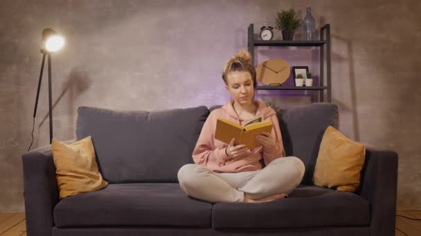 Na pohovce sedí mladá žena a čte si knihu. Ten muž dal dar své milované.. — Stock video