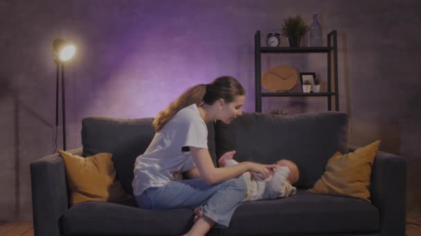 En kvinna leker med sitt barn i soffan i en mysig lägenhet. Mamma och barnet är lyckliga. — Stockvideo