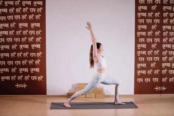 Joven mujer atractiva deportista practicando yoga, meditando en pose de yoga, haciendo ejercicio, usando ropa deportiva, estudio de yoga ligero — Foto de Stock