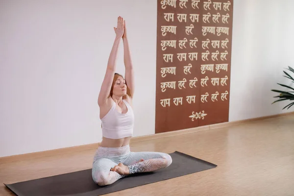 Joven mujer atractiva deportista practicando yoga, meditando en pose de yoga, haciendo ejercicio, usando ropa deportiva, estudio de yoga ligero — Foto de Stock
