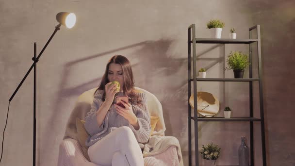 A young and beautiful woman is sitting in a chair and writing a message on her phone — Stock Video